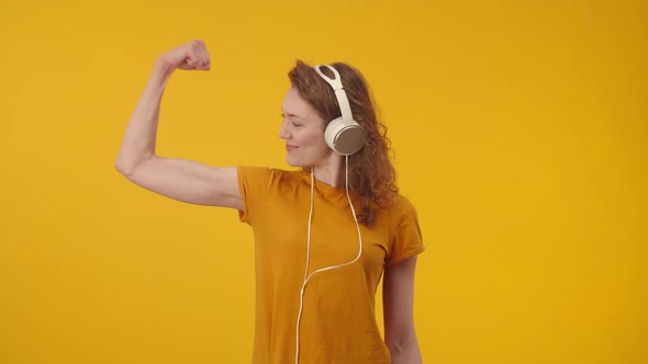 Happy Woman in Headphones Smiles and Shows Biceps on Hands alt