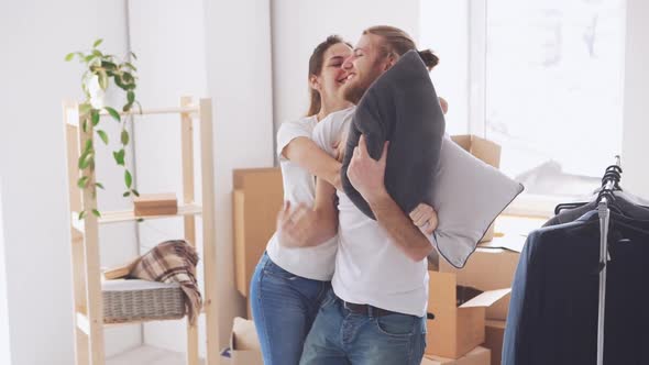 Smiling Caucasian Pair Having Pillow Fight in Their New Flat and Kissing Each Other in Slowmotion alt