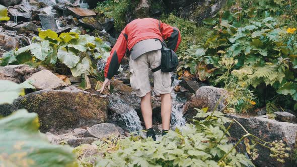Tourist Collects Water in a Plastic Bottle From a Mountain Stream. Hiking Adventure alt