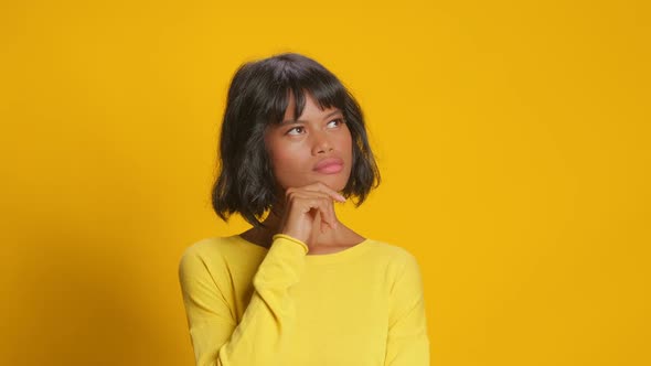Young Woman Looks Somewhere Pensively Thinks Deeply Against Yellow Background alt