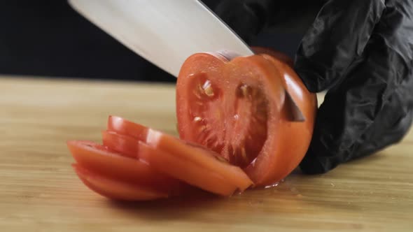 Chef in Black Gloves Cutting Fresh Tomato Into Slices on Wooden Board Closeup