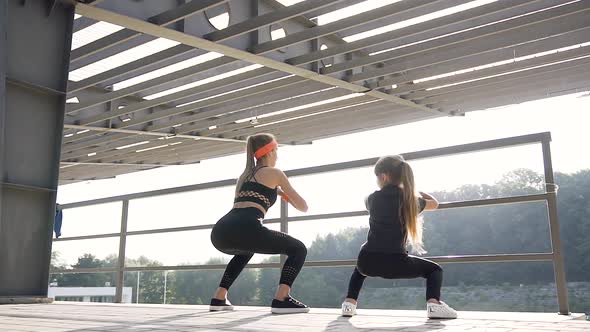 Young Woman and Little Girl which Doing Together Squat Exercises Near Handrail alt
