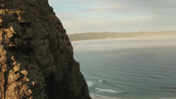 Aerial flying around cliff face to reveal huge sand bay at sunrise alt
