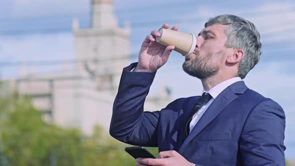 Middle-aged man drinking tea and messaging on smartphone