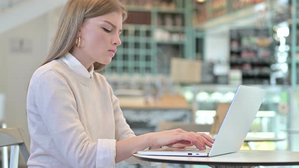 Thoughtful Young Woman Working on Laptop in Cafe alt