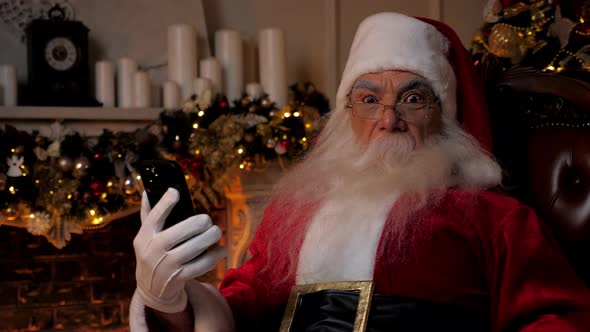 Shocked Santa Claus Looks at Smartphone Turns Head in Surprise Looks Camera alt