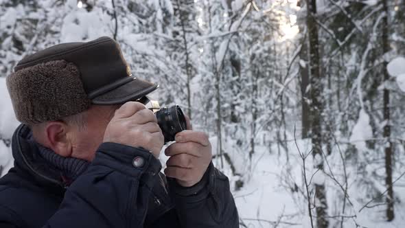 Elderly Man Is Photographing Forest at Winter Walking in Snowy Woodland at Daytime alt