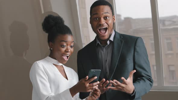 Young Excited Amazed African Colleagues Looking at Smartphone Screen Feel Overjoyed Euphoric with alt