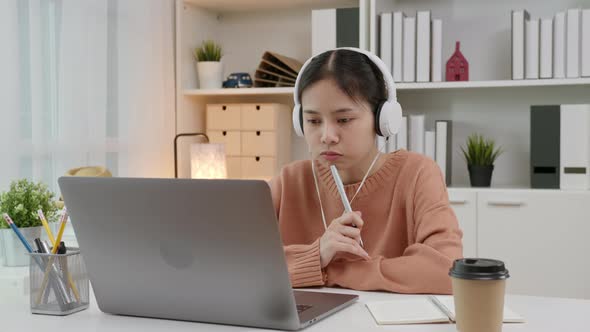 Young Asian girl learning by online lesson at home and chatting on laptop with teacher