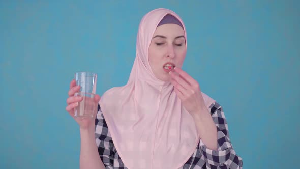 Young Beautiful Muslim Woman with a Pill and a Glass of Water Taking a Pill alt