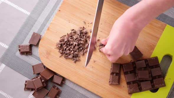 Woman Chopping Black Dark Chocolate on Wooden Cutting Board alt