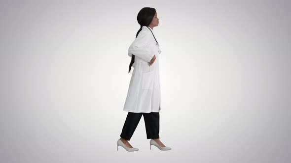 Sad African American Female Doctor Walking with Hands in Her Pockets on Gradient Background alt