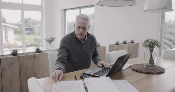 Senior adult male doing domestic finance on laptop at home on table, day in life