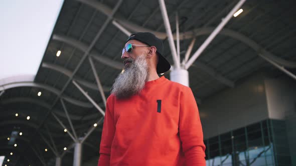 Portrait of Handsome Stylish Mature Man with Long Gray Beard Wearing Cap and Sunglasses on Urban alt