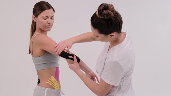 A female physiotherapist is measuring a piece of kinesiotape to be applied on a shoulder joint alt