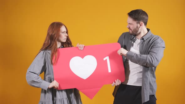 Man and a Woman are Fighting for Attention on Social Networks They are Holding a Like Sign They are alt