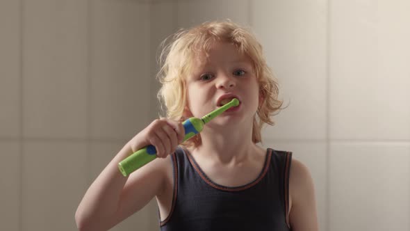 Little Blond Boy Diligently Brushing his Teeth with Electric Toothbrush