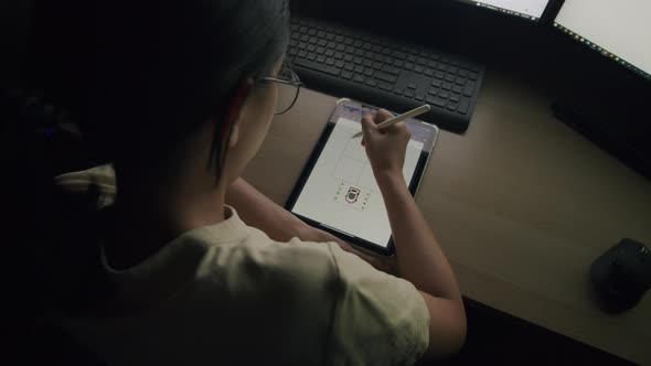 Young Asian female sketch work on a tablet at night in a home office.