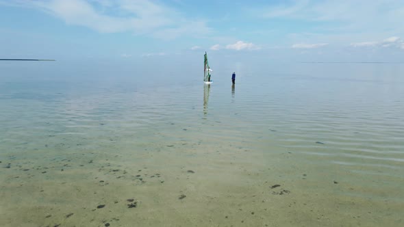 Aerial View Drone Following Surfer Instructor Teaching Person Windsurfing on Calm Sea Water alt