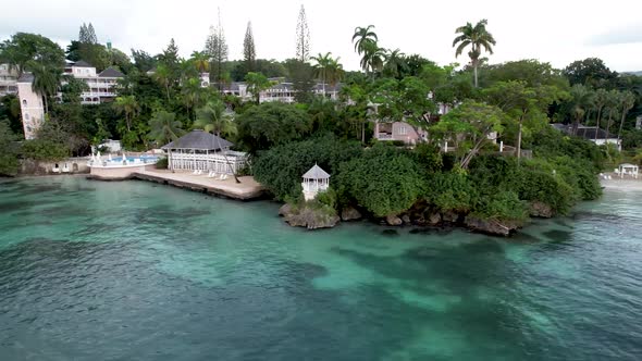 Aerial view of tropical resort along coastline with pool, beach and palm trees alt