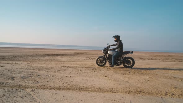 Motorcyclist Driving His Customized Fast Motorbike on the Dirt Road in Desert Around Sea or Lake alt