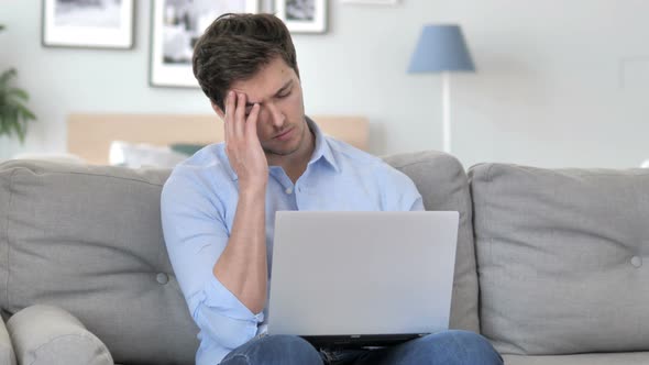 Young Man with Headache Sitting on Couch with Laptop alt