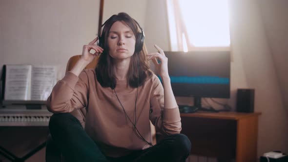 A beautiful girl with big headphones listens to music in a chair at the computer, dances
