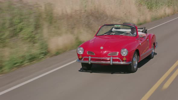 Tracking shot of man driving classic convertible car on country road.  Fully released for commercial