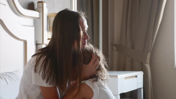 Young Mother Caresses Her Little Daughter in Bedroom at Home alt