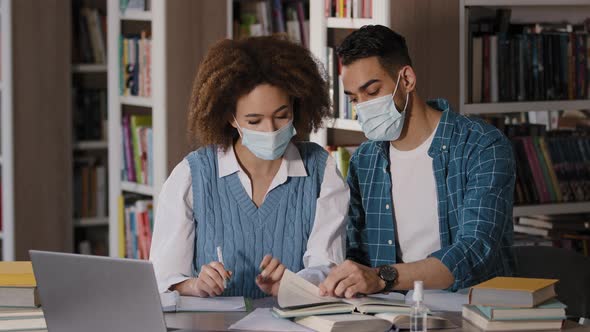 Two Students Girl and Guy in Protective Masks Sitting at Desk Listening to Online Lecture From alt
