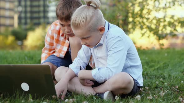 Cute Caucasian Boys Sitting Ongrass in Park with Laptop Computer Doing Homework alt