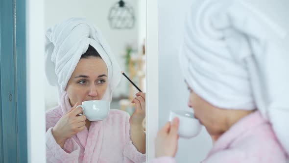 Young Woman Applying Makeup and Drinking Coffee alt