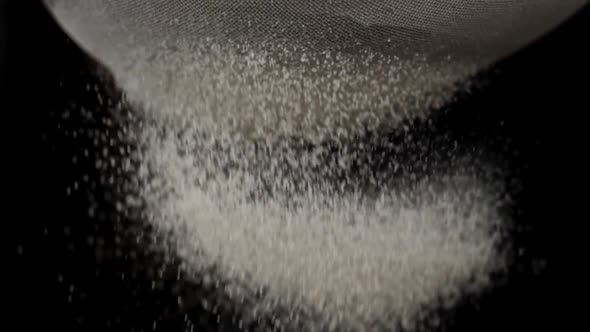 Closeup of White Flour is Falling Through a Steel Sieve on Black Background