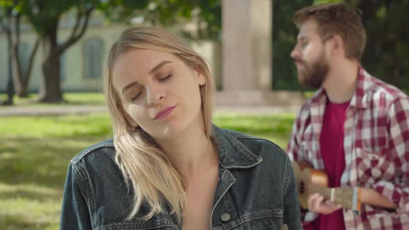 Close-up Face of Young Blond Woman Listening To Music and Smiling. Blurred Romantic Man Playing alt