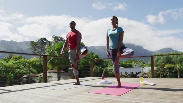 Relaxed biracial couple on terrace, practicing yoga together on mats alt