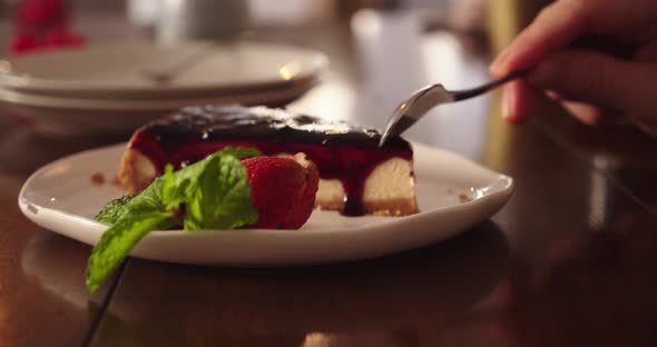 Cheesecake on a White Plate Drizzled with Blueberry Jam on Top Garnished with Strawberries and Mint alt
