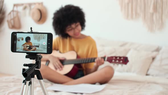 Afro American Woman Blogger Teaching Guitar Lessons Using Smartphone alt