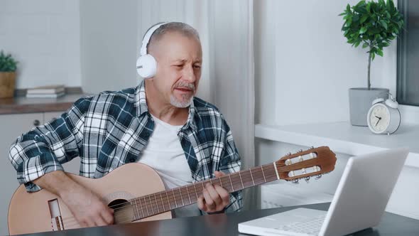 A Man Plays the Guitar Sitting in Front of a Computer at Home