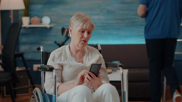 Senior Person Sitting in Wheelchair and Using Smartphone alt