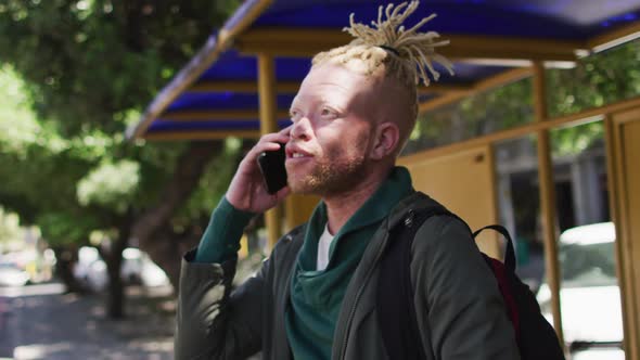 Happy albino african american man with dreadlocks in park talking on smartphone alt