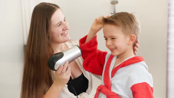 Portrait of Little Boy and Young Mother Drying Hair with Hairdryer in Bathroom alt