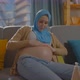 Pregnant Muslim Young Woman Uses Ointment or Body Lotion Sitting in the Living Room at Home - VideoHive Item for Sale