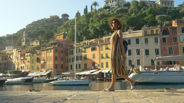 A woman walking wearing hat and backpack purse traveling, Portofino, Italy, luxury resort, Europe. alt