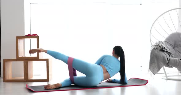 Fitness woman doing leg raises exercise for glute with resistance band at home.
