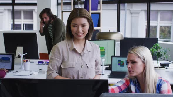 Diverse business people standing talking using computer in modern office alt