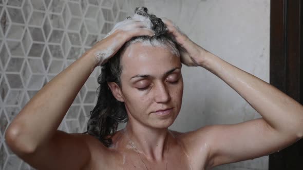 Young Woman is Washing Her Hairs with Shampoo Taking a Shower with Close Eyes
