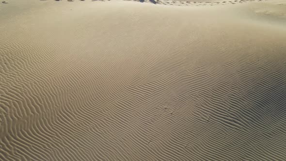 Drone Flying Over Sand Dunes with Two People Sitting at the Edge