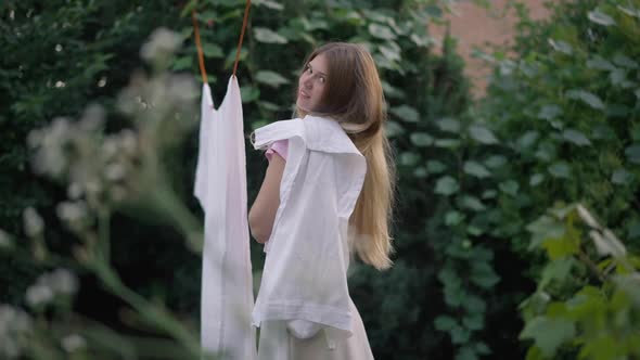 Side View Young Slim Woman Hanging Clean Fresh Laundry on Shoulder Smiling Looking at Camera alt