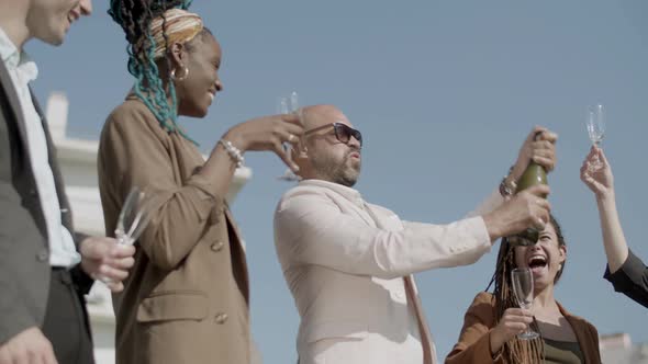 Happy Employees Opening Champagne with Splashes During Party alt