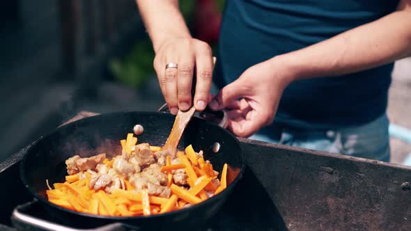 CU: Young Man, Standing Near the Brazier, Mixes Pork and Carrots with Onion, Wooden Spatula alt